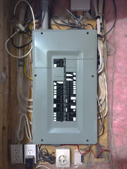 Vertical view of a residential electrical panel, surrounded by exposed wiring, outlets, and pink insulation, highlighting home electrical infrastructure.