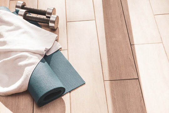 Home workout setup with dumbbells, exercises mat and glass of water in natural sunlight. Cozy fitness corner for self-care, morning exercises and healthy lifestyle