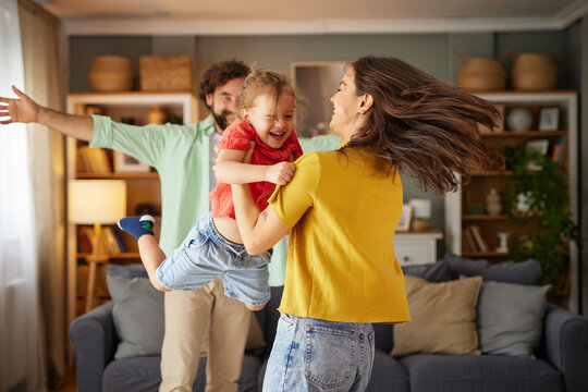 A cheerful family is having fun at home, with laughter filling the air as the mother lifts her daughter while the father joins in the celebration.