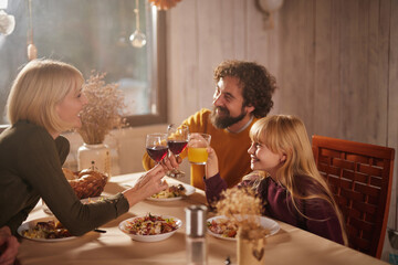 A cozy autumn dinner features a family joyfully toasting with drinks at a beautifully set table. Plates of food and warm lighting create a welcoming atmosphere.