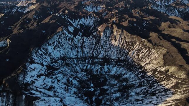 Aerial view of jagged mountains blanketed in snow, creating a stark contrast between the dark rock and the glacial ice, Vik, Myrdalshreppur, Iceland.