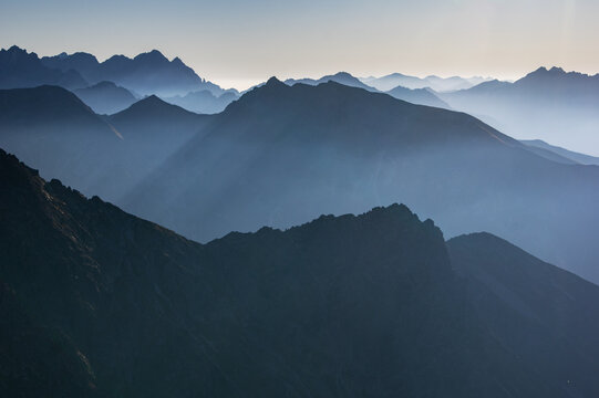 Aerial view of the majestic, mist-veiled High Tatras mountains, where shadowy peaks rise in layers under a serene sky, as viewed from Jahnaci stit inVysoke Tatry, Presov Region, Slovakia.