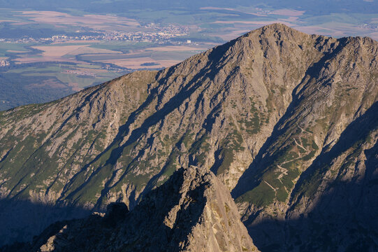 Aerial view of the rugged, sun-drenched Jahnaci stit peak casts long shadows over the landscape, a tapestry of textures and tones, Vysoke Tatry, Presov Region, Slovakia.