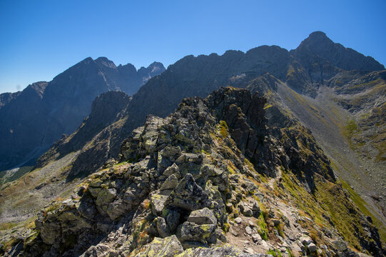 Aerial view of jagged peaks ascend towards a clear blue sky, casting long shadows across the rocky terrain of Jahnaci stit peak, Vysoke Tatry, Presov Region, Slovakia.