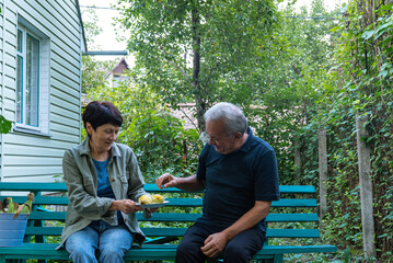 A middle-aged couple sits on a green bench in their lush garden
