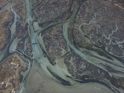 Aerial view of sinuous waterways carve through the landscape, creating a mosaic of textures where earthy browns meet the shimmering turquoise of the water, Carnota, A Coruna, Spain.