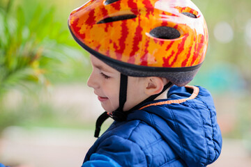 Close-up of a young boy wearing a brightly colored safety helmet, looking down or away with a...