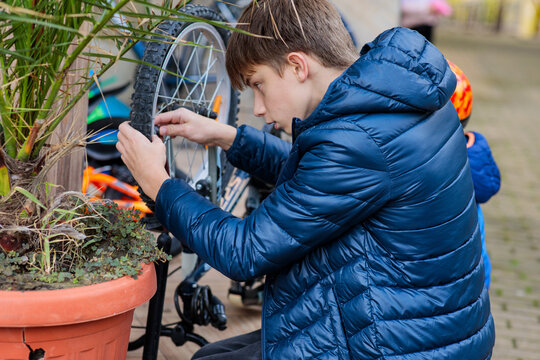 Focused teenage boy repairing a bicycle tire, using a hand pump or checking the valve on an outdoor patio in autumn