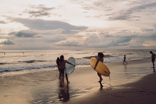 Three surfers step into shallow surf with boards, starting a session as evening lights the clouds. The scene focuses on equipment, stance, and teamwork, capturing movement, practical coastal training