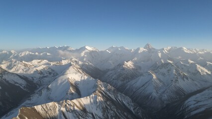 Aerial view of majestic snow-covered mountain peaks stretching into the distance under a clear blue sky, showcasing the rugged terrain and natural beauty of the landscape