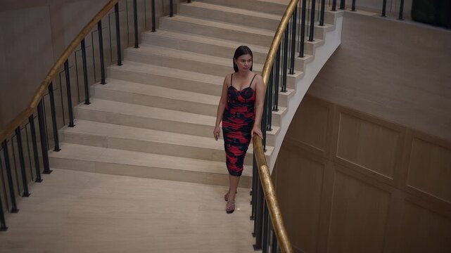woman in striking red dress confidently walking down sweeping grand staircase during special event