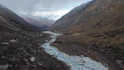 Expansive mountain valley features a winding river flowing through rocky terrain, surrounded by majestic peaks and sparse vegetation, creating a tranquil and picturesque natural scene