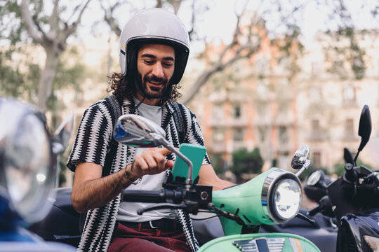 Young man uses smartphone while seated on scooter, smiling confidently, reflecting joy, control and independence enabled by mobile tech and digital navigation tools.