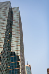 Obraz premium Vertical upward view of a reflective glass office tower in natural daylight. Clear blue sky fills the right side of the frame. Strong geometric architectural lines.