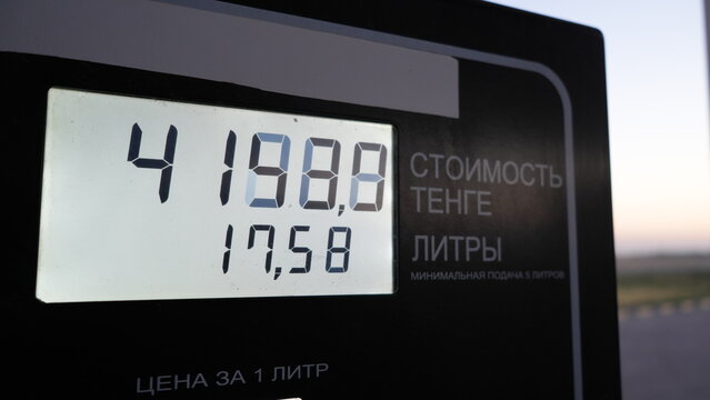 Digital fuel price display shows cost per liter in a gas station setting, illuminated against a soft sunset backdrop. Text: Price in tenge, Liters, Price per liter