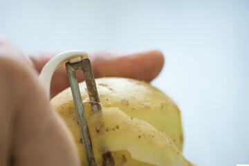 Closeup photo of male hand peeling raw potatoes with special knife. Sharp peeler slicing raw potato, close-up of food prep tool in use