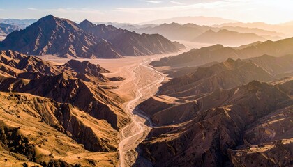 An expansive desert landscape unfolds with dramatic, sun-drenched mountains and a dry, winding riverbed stretching into the distance.