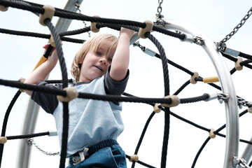 Dziecko wspinające się po linowej konstrukcji na placu zabaw © Przemysaw