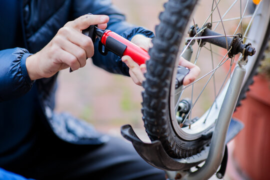 Close-up of a child's hands using a red hand pump to inflate a flat bicycle tire, showing repair and self-reliance outdoors