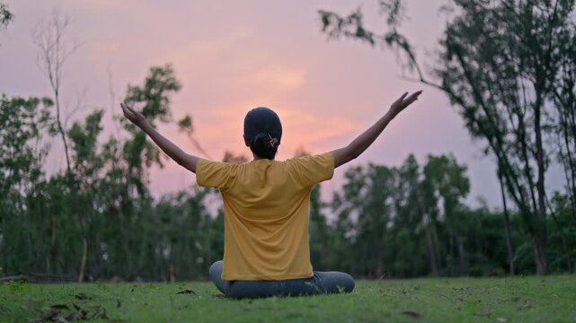 Rear view of a woman practicing prayer pose at outdoor in early morning light, expressing serenity, wellness, and healthy living.