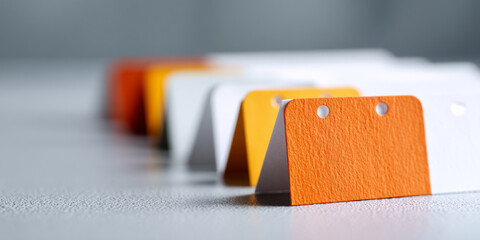 Close-up of colorful paper swatches arranged in a row on textured surface with shallow depth of field and focus on orange swatch