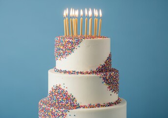A festive threetier birthday cake adorned with colorful sprinkles and lit candles against a vibrant blue background, perfect for celebrations