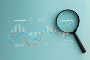 Magnifying glass over digital data graph and charts. Business analytics, financial market research, and statistics concept. Stock market, investment, and data audit.