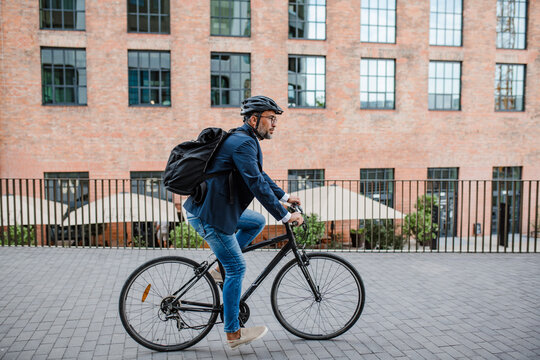 Side view of businessman riding bike to office, wearing backpack and helmet.