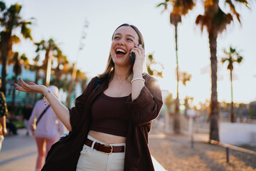 Laughing young woman talking on smartphone outdoors, expressing joy and energy, symbolizing modern communication, digital lifestyle, mobile connection and cheerful technology use.
