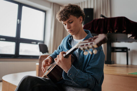 Teenage boy playing acoustic guitar in school music room.
