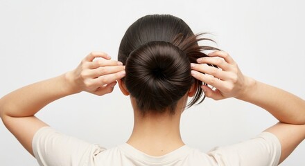 Rear view of a woman styling her dark brown hair into a neat donut bun. Female creating a classic updo hairstyle. Hair care and beauty concept