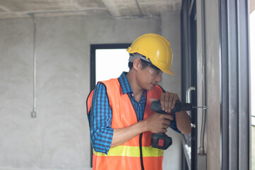 A construction worker is using a large,  hammer drill screwing  a screw into the wall using a cordless screwdriver
