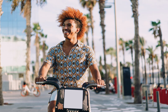 Close-up of smiling young man on rental bicycle, enjoying ride. Conceptual image representing urban eco-commuting, digital mobility, and app-based transportation lifestyle. - Powered by Adobe