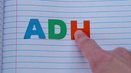 ADHD. A person spelling the word ADHD out of letters on a notebook sheet. Close up.