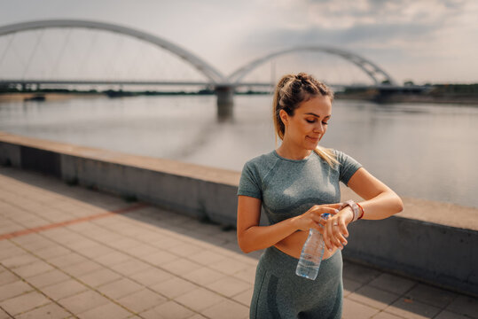 Young sportswoman checking smartwatch near river after training - Powered by Adobe