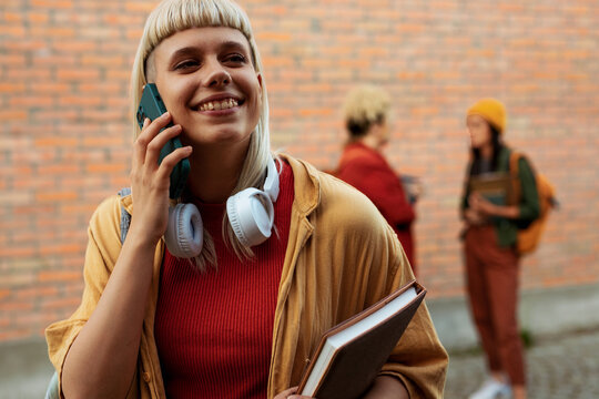 Smiling student woman calling on phone at university campus - Powered by Adobe