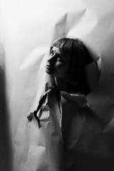 A person emerges from torn paper, gazing upwards with a look of contemplation. The stark black and white creates a dramatic contrast, highlighting the struggle for freedom and self-expression