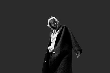A figure in a black coat and gray hoodie poses confidently in a dimly lit urban space. The atmosphere reflects modern style and bold expression, creating a strong visual impact