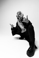In a minimalist studio setting, a person strikes a dynamic pose wearing a hoodie and oversized coat. Their playful expression and gesture radiate confidence and creativity, embodying urban fashion