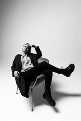 A person sits confidently in a sleek chair, wearing a cozy hoodie and stylish coat. Their pose exudes a sense of relaxed sophistication against a neutral backdrop