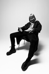 A person sits comfortably in a sleek chair, exuding confidence and style. Clad in dark clothing and statement boots, the mood is artistic and bold, highlighting personal expression