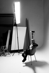 In a well-lit studio, a person sits casually in a stylish chair, framed by soft light and minimalist decor. The atmosphere is relaxed yet professional, perfect for artistic expression