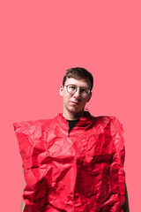 A young person stands confidently against a bright pink background, wearing a unique, crumpled red outfit that adds a playful, artistic flair to the scene