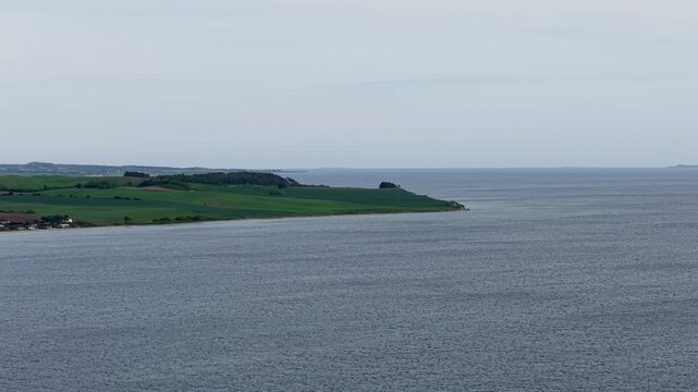 Aerial view of calm coastal waters meeting the green, rolling shoreline of Mols Bjerge National Park in Denmark