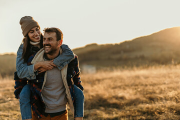 Happy couple enjoying piggyback ride in nature at sunset