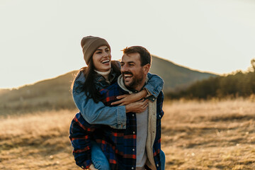 Happy couple enjoying piggyback ride in nature at sunset