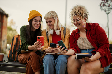 Diverse students laughing, sharing content on smartphones outdoors