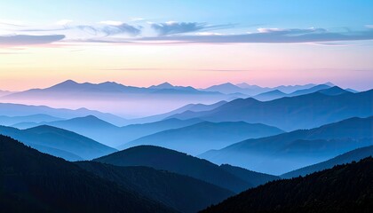 A vast mountain landscape unfolds with multiple layers of blue-hued peaks fading into a soft, pastel-colored sky at sunrise.