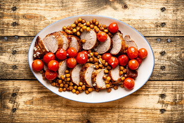 Roast pork tenderloin served with chickpeas and tomatoes in plate