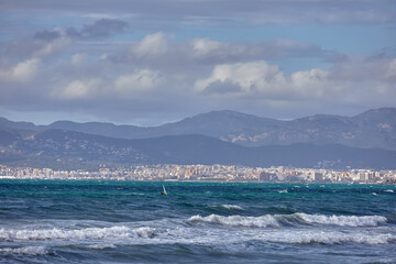 Windsurfer riding waves on a windy day with a scenic view of the city and mountains in the background. coastal landscape